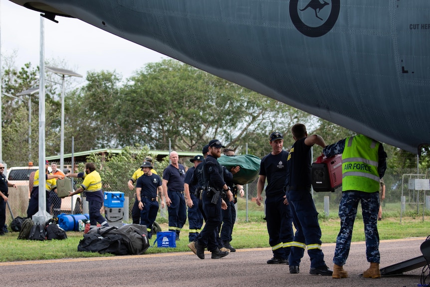 A group of people, some in defence force and emergency service uniforms, load goods onto a large military helicopter.