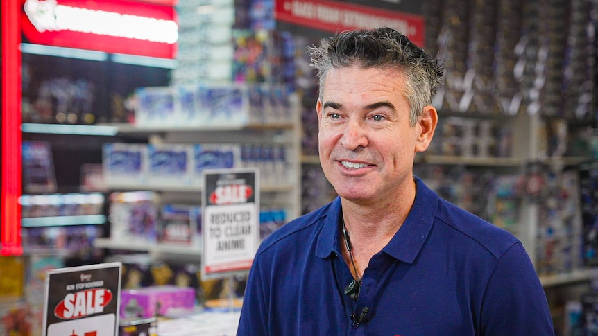 A man with grey hair and a blue polo shirt, standing inside a toy shop.