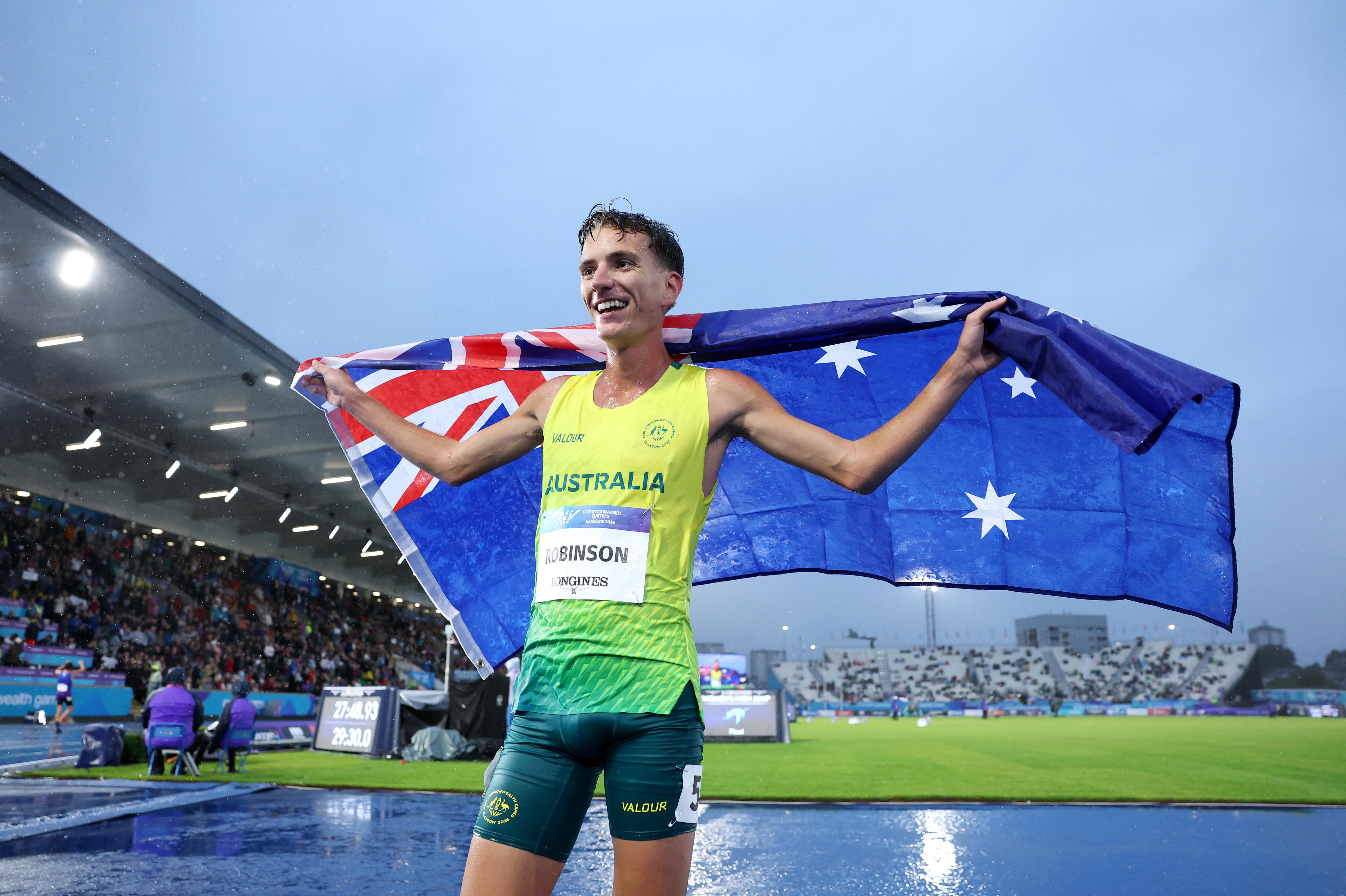 A man in green and gold holds an Australian flag