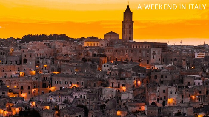 A photograph of a medieval Italian city at dusk with the words 'A Weekend in Italy' in white text in the right-hand corner.