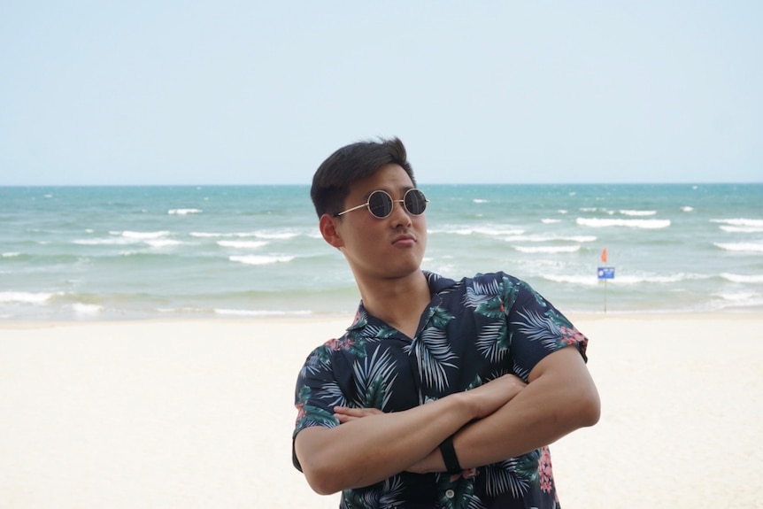 A male wearing sunglasses standing on the beach