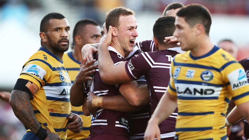 NRL players embrace after a try, while their dejected opponents stand around watching.