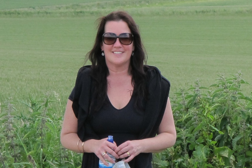 A woman with sunglasses standing in a green field.
