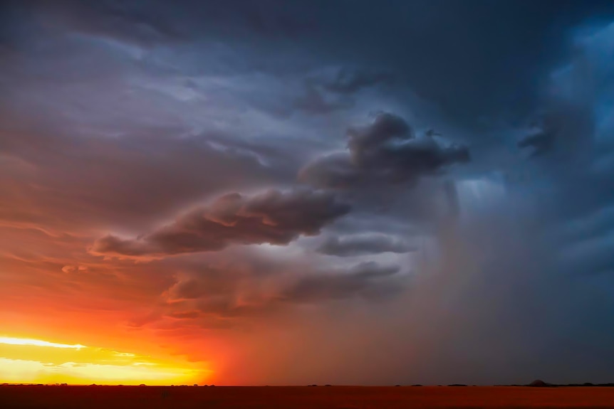 Dark storm clouds fill the landscape over a setting sun in the desert.