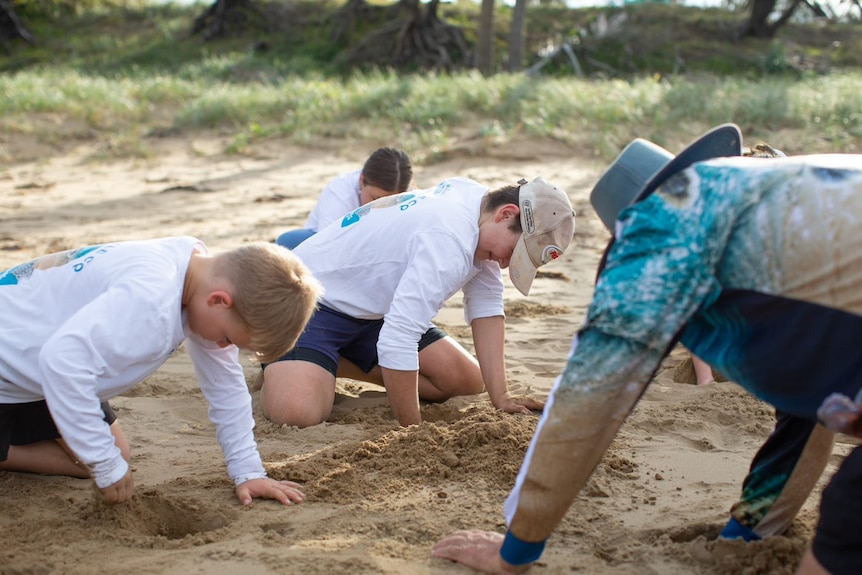 Two kids in white shirts digging in the sand at the beach