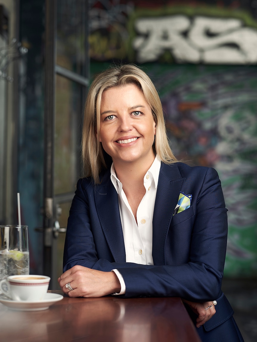 Business woman poses with a smile. She's sitting at a table with a cup of tea and saucer in front of her