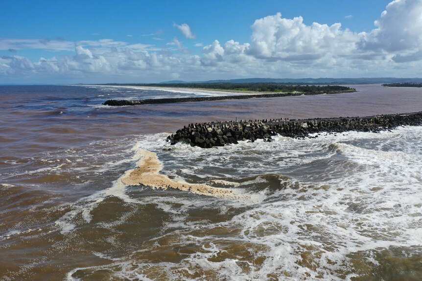 A wide shot of a river flowing into the ocean with dirty brown water and dirty foam.