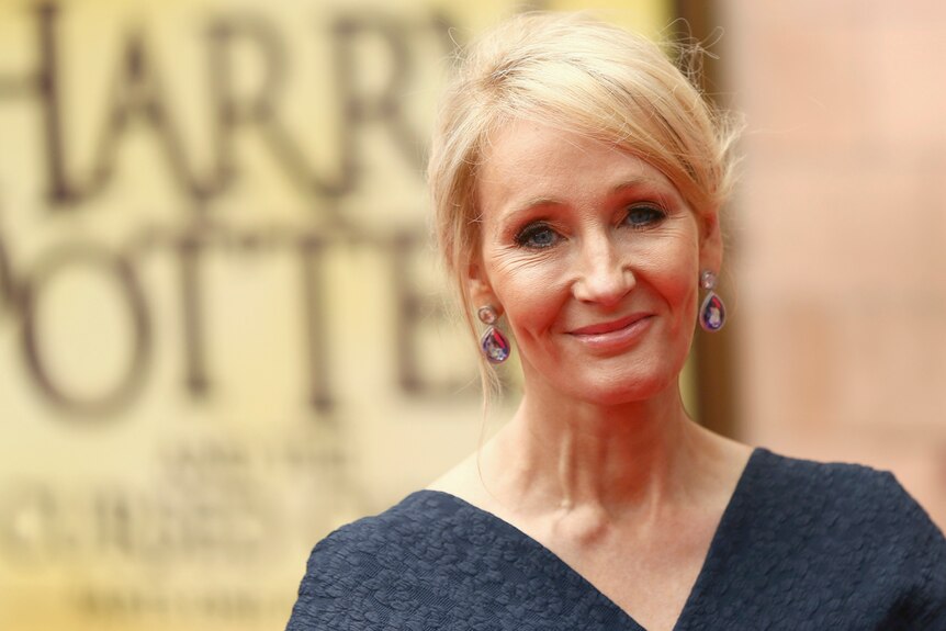Author JK Rowling in front of a yellow Harry Potter poster at a gala performance in London.
