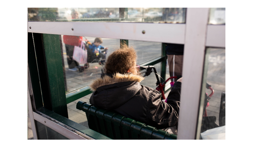 A woman sits at a bus stop and waits.