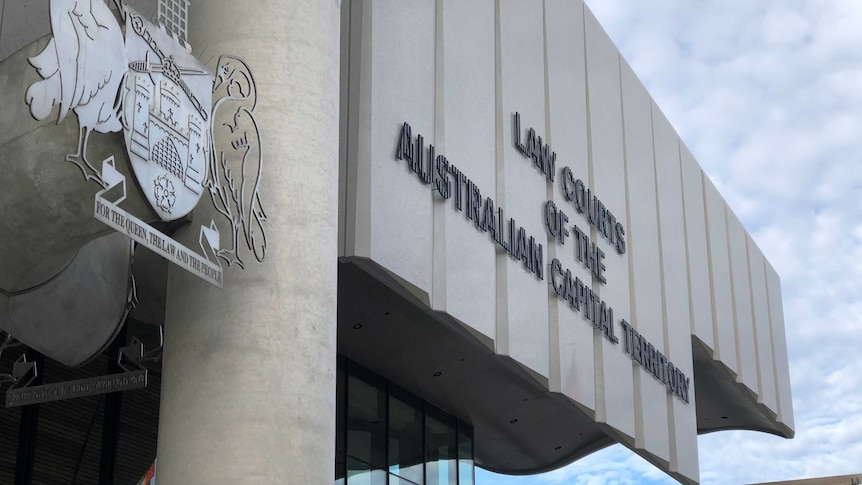 The sign out of the front of the building and the crest, with an autumnal tree nearby and a blue sky beyond.