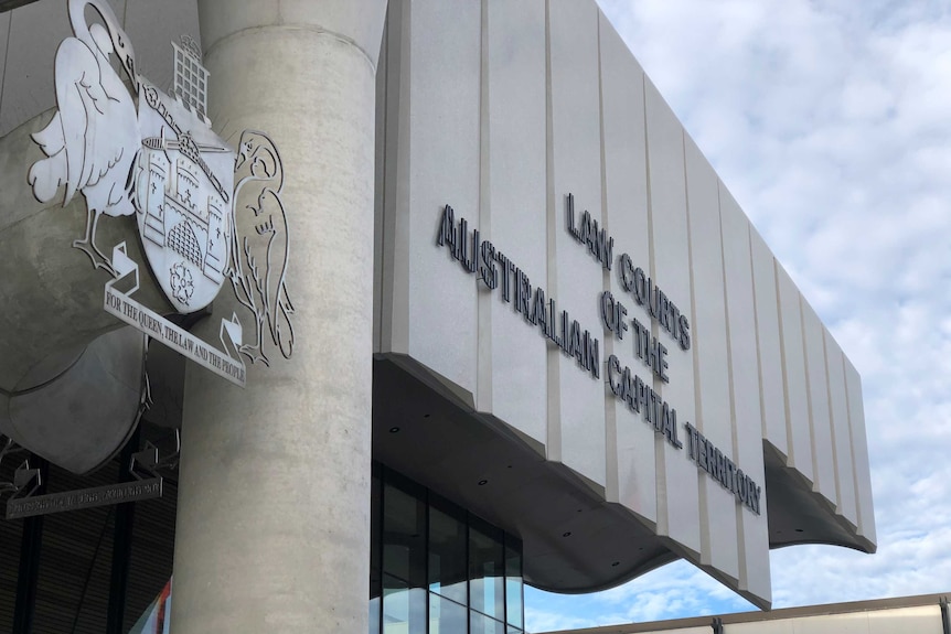 The sign out of the front of the building and the crest, with an autumnal tree nearby and a blue sky beyond.