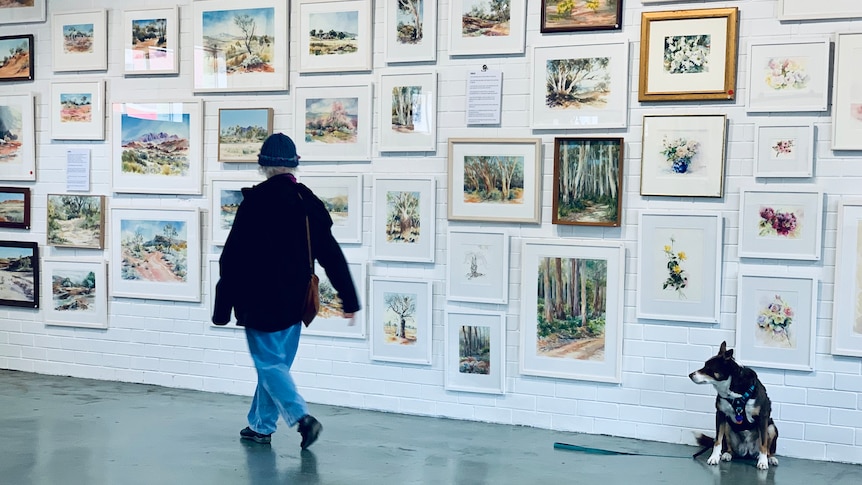 a woman walks past a gallery wall filled with framed paintings