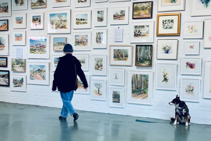 a woman walks past a gallery wall filled with framed paintings