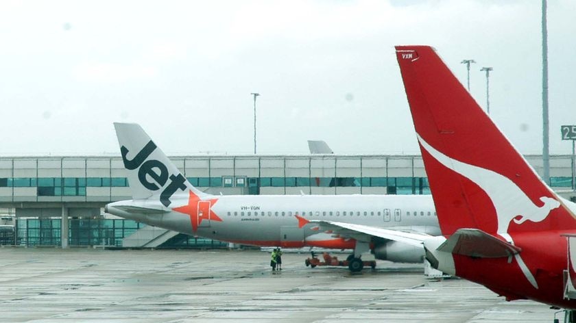 Jetstar and Qantas planes next to each other on the tarmac at an airport.