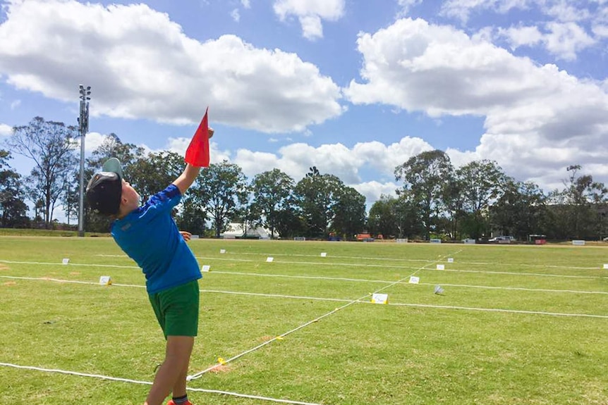 Young boy throws a red paper plane.