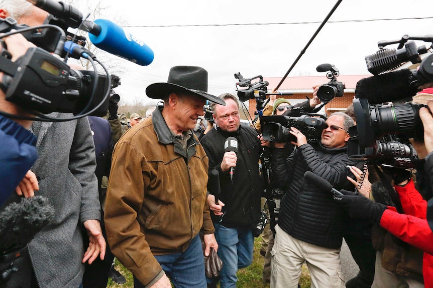 US Senate candidate Roy Moore is surrounded by journalists and TV cameras.