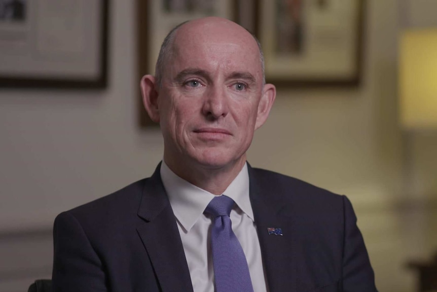 Stuart Robert sitting in his office, wearing a dark blue suit and blue tie.