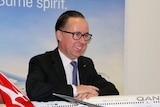 Qantas CEO Alan Joyce rests his arms on a Qantas plane model.