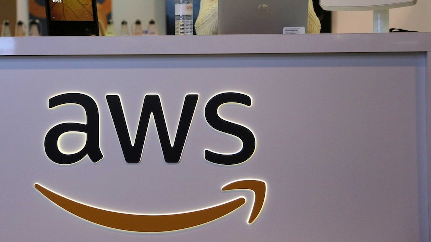 A woman stands behind a desk with the Amazon Web Services logo across the front.