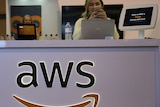 A woman stands behind a desk with the Amazon Web Services logo across the front.