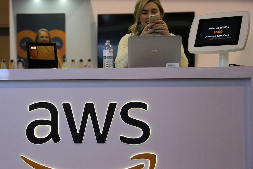 A woman stands behind a desk with the Amazon Web Services logo across the front.