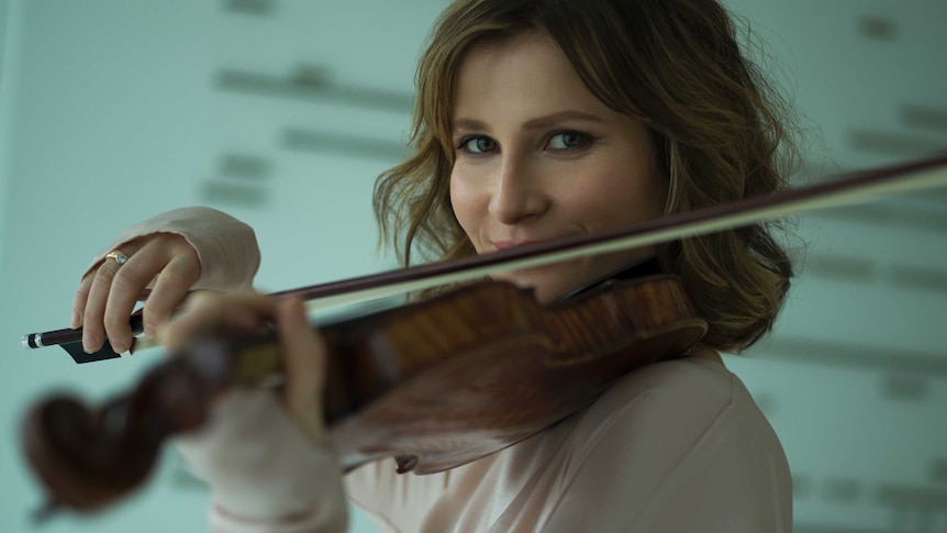 A woman plays violin looking directly at the camera.