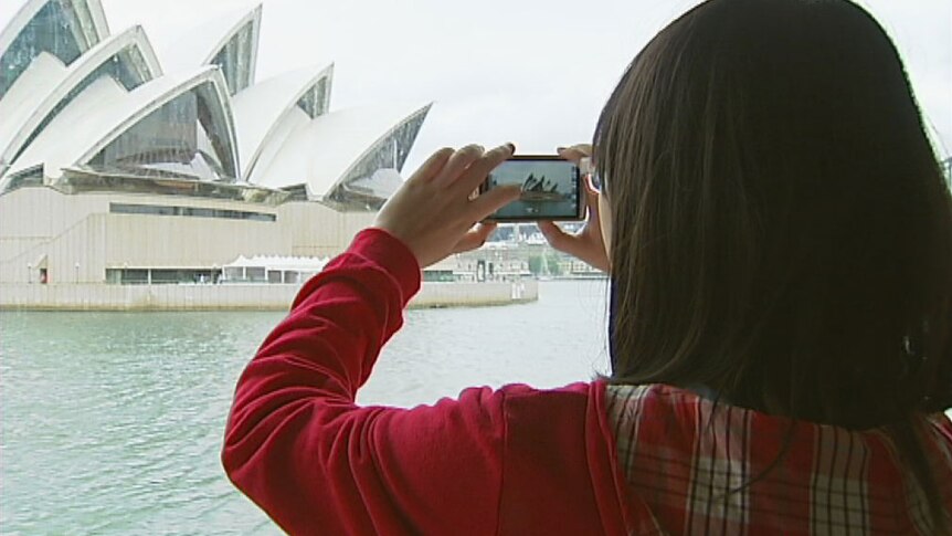 Unidentifiable tourist takes photo of the Sydney Opera House.