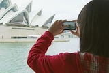 Unidentifiable tourist takes photo of the Sydney Opera House.