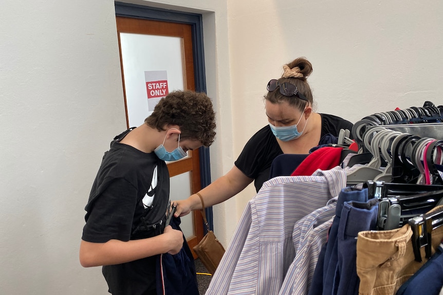 A woman and a boy looking at school pants near a rack. 