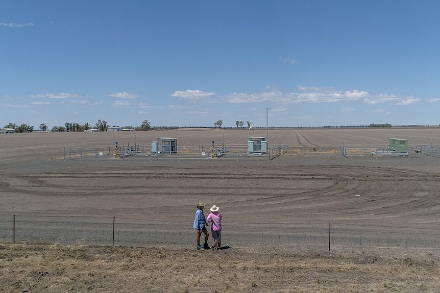 Zena and Gary Ronnfeldt stand at fence look at gas wells on the property next door at their farm near Dalby, Queensland, 2020.