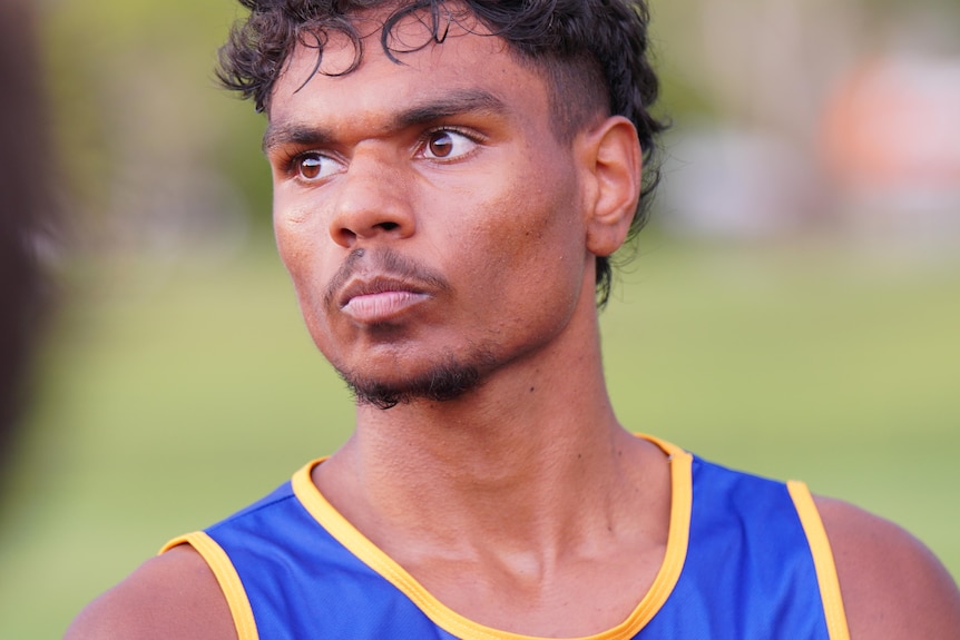 A young Aboriginal man looks away from the camera. He is wearing a football jersey. 