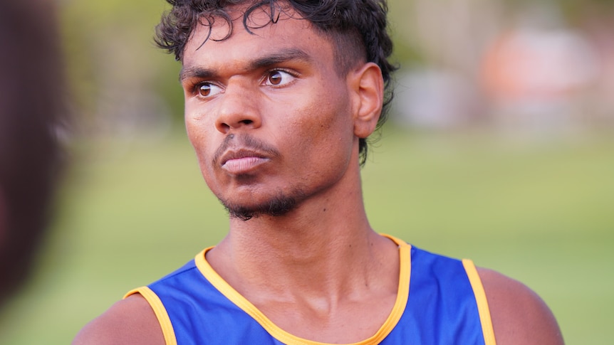 A young Aboriginal man looks away from the camera. He is wearing a football jersey. 