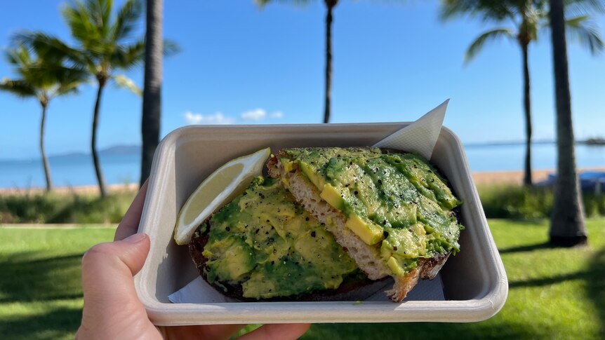 hand holds avocado toast with a tropical background