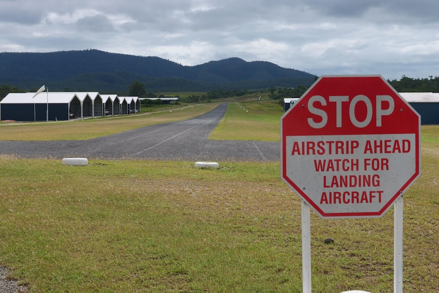 A small airfield in the background with a sign in the foreground which says Stop airstrip ahead watch for landing aircraft.