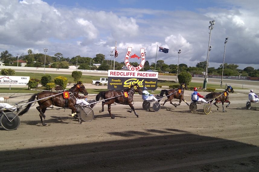 A day time shot of a harness race at the paceway.