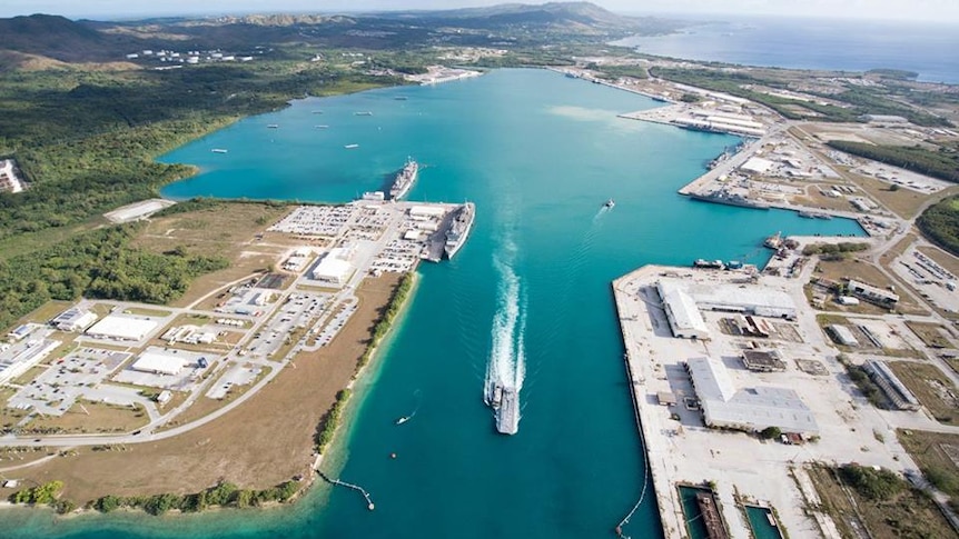 An aerial image of the US Naval Base in Guam showing buildings spread across land and boats in parts of the bright blue water. 