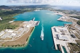 An aerial photo shows a naval base perched on either side of a wide harbour sitting on the end of a tropical island.