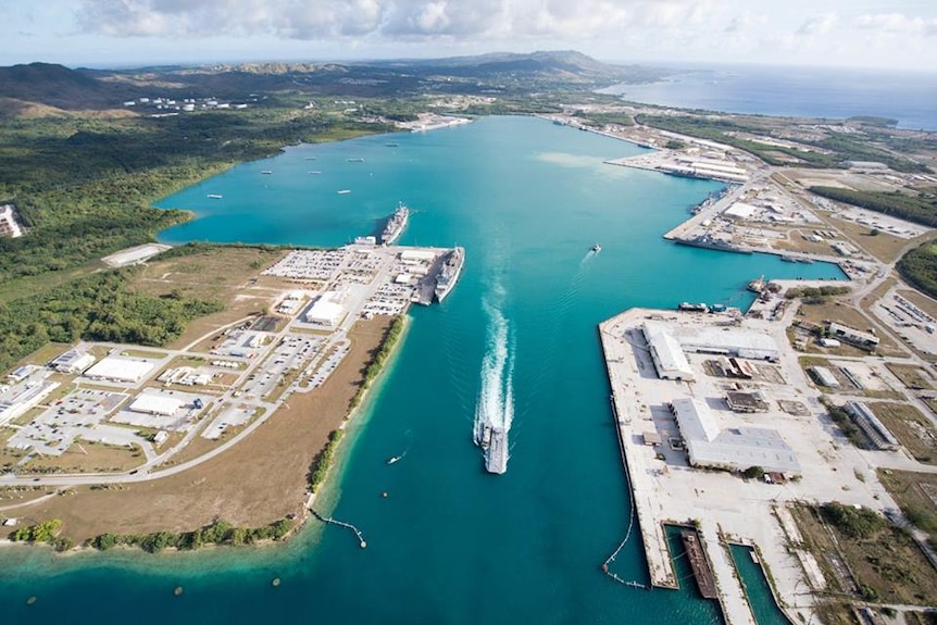 An aerial photo shows a naval base perched on either side of a wide harbour sitting on the end of a tropical island.