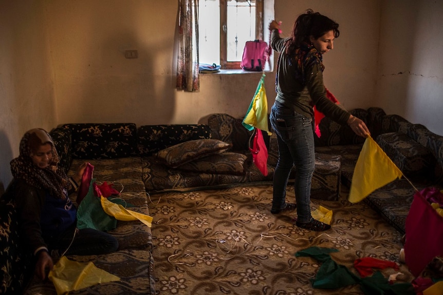 Two women in a lounge room put flags up on the wall