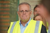 Scott Morrison wearing a yellow high vis vest in front of microphones at a press conference