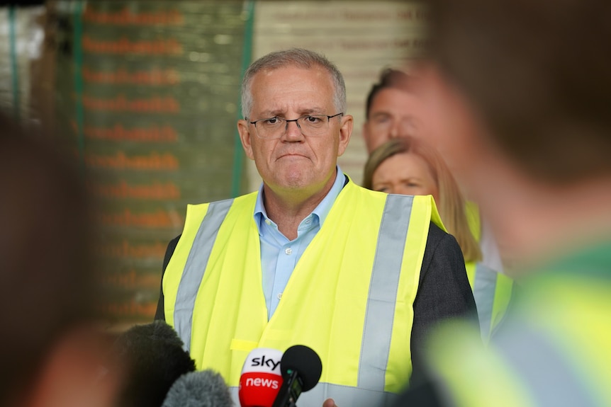 Morrison grimaces while holding a press conference while wearing a high-vis vest.