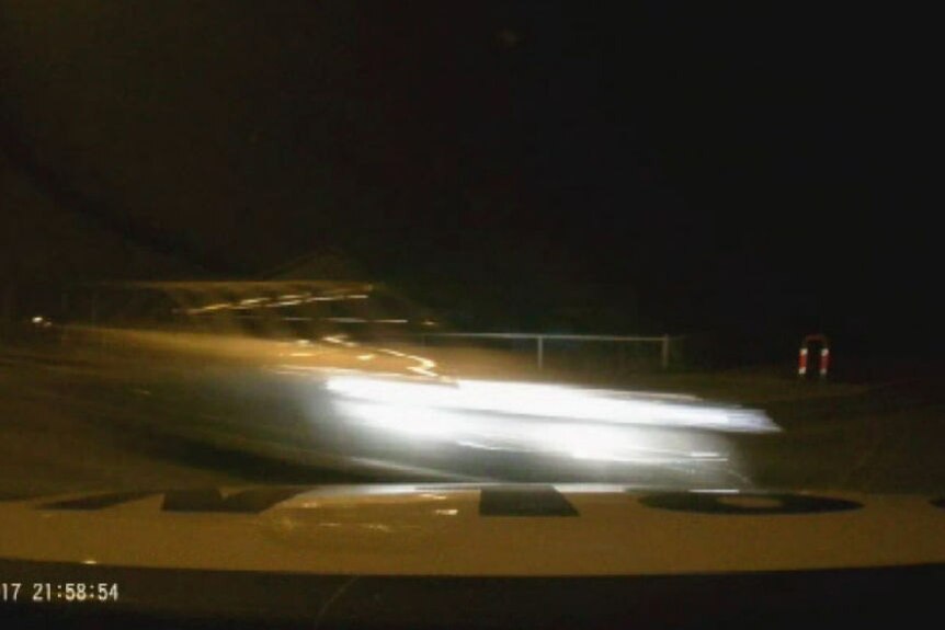 A car speeds past a police vehicle at night.