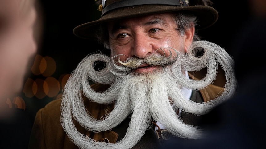 A man with multiple curled strands of his white beard form an octapus shape at a competition 