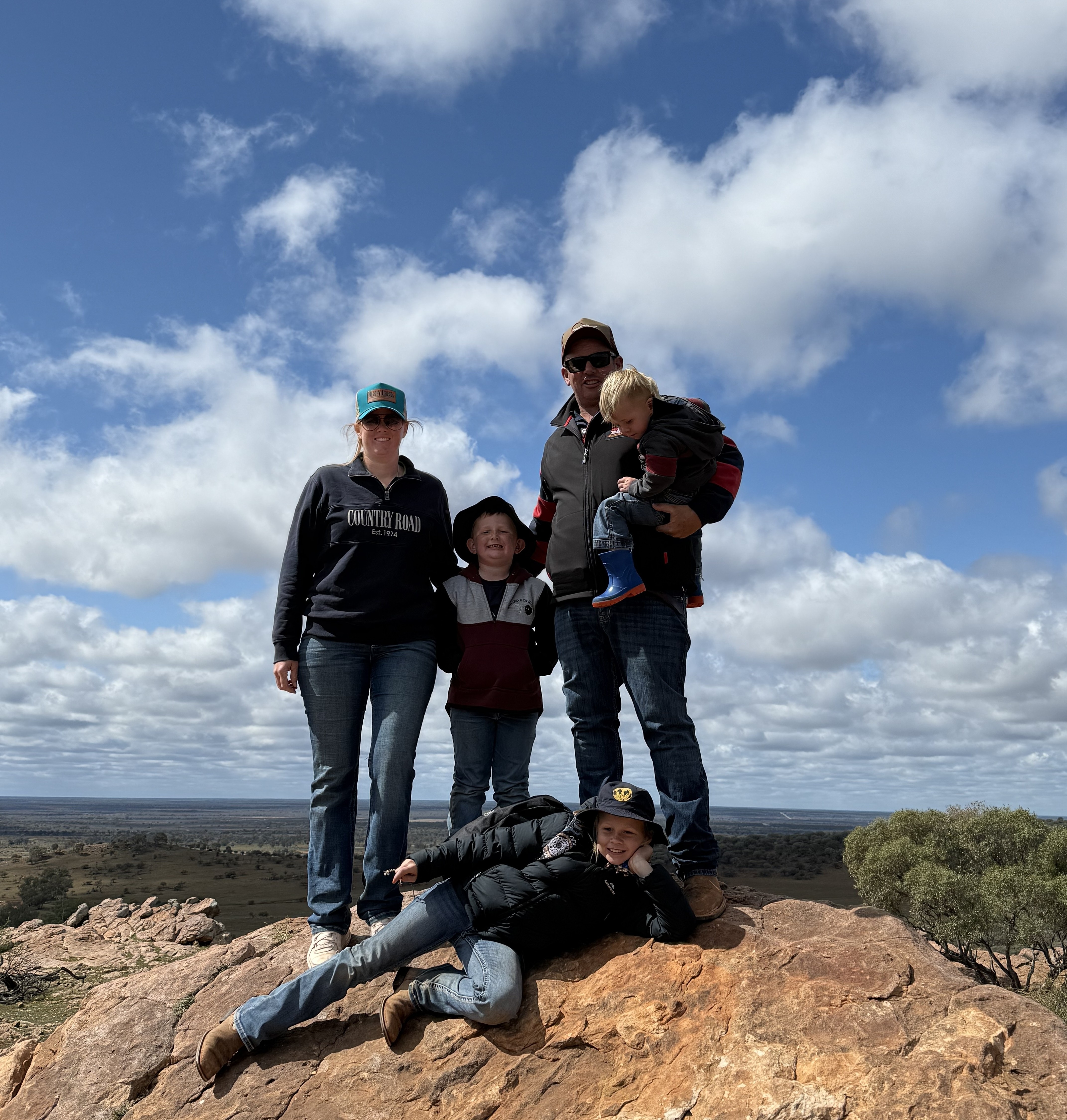 Family of five standing on a rock, dressed in jeans and jackets.
