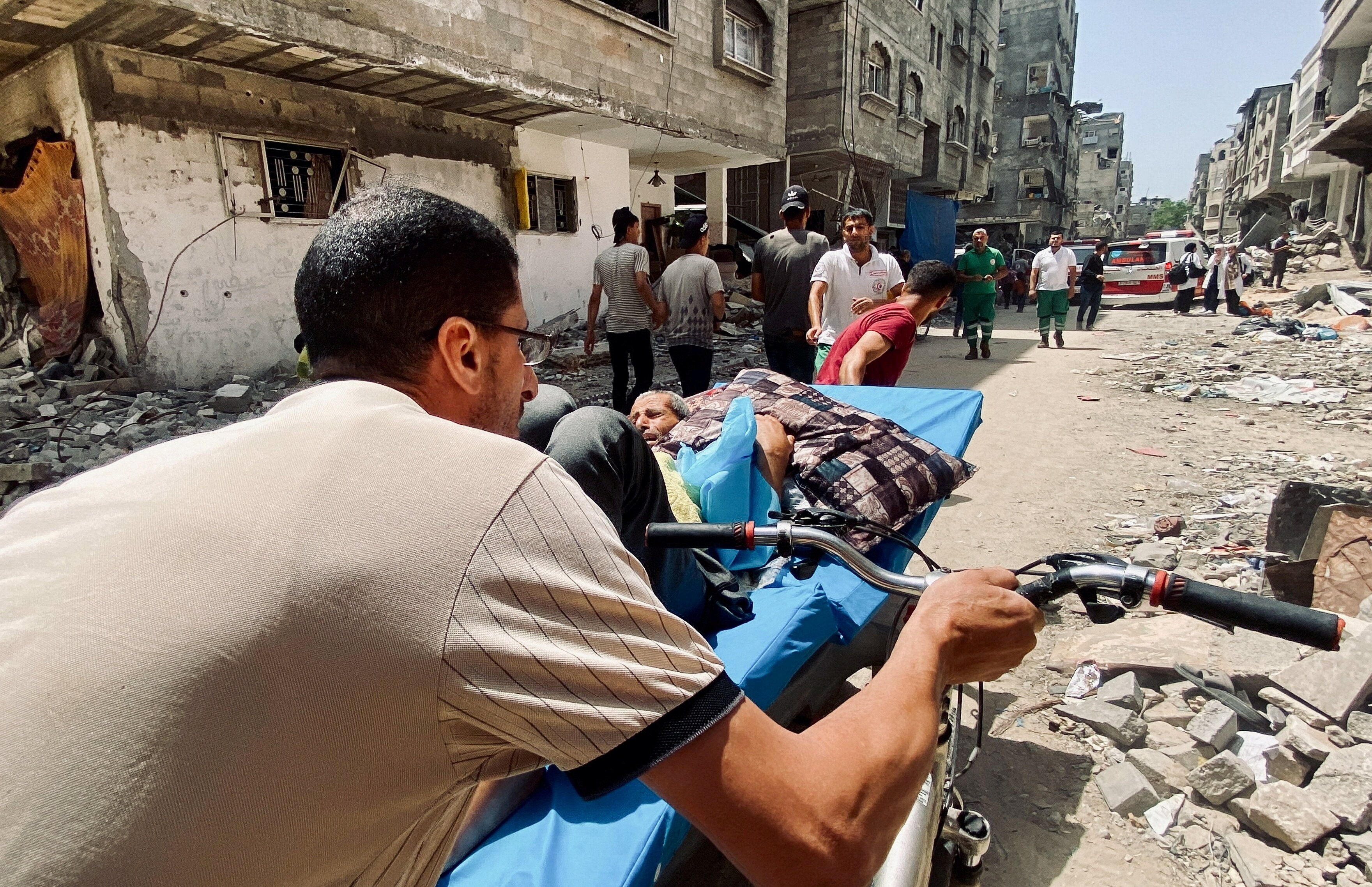 Two men push a patient on a hospital bed through rubble 