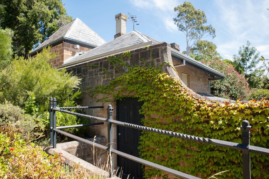 A sandstone house sits among trees and vines.