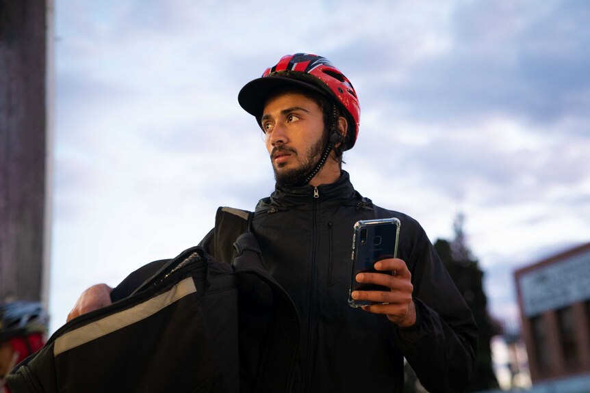 A man with a bicycle helmet on holding a mobile phone.