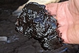 A close up of a hand with a black sludge on its fingers. 