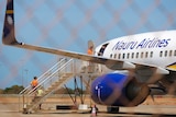 A Nauru Airlines plane on the tarmac at Broome Airport, viewed through a cyclone fence with a staircase attached,