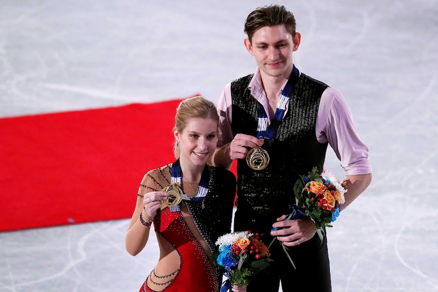 Windsor and Alexandrovskaya stand with their gold medals and flower bouquets on the ice at the world juniors